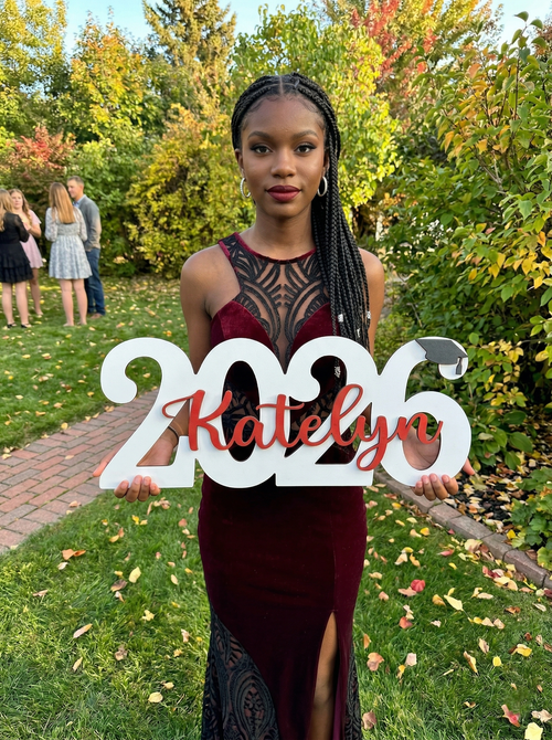 Woman holding a '2026 Katelyn' sign outdoors with greenery in the background