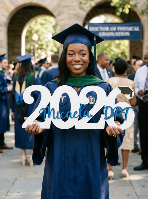 Graduate in cap and gown holding '2023' sign with name and degree details, outdoors.