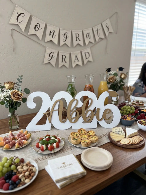Graduation-themed table setting with 'Congrats Grad' banner and personalized '2026 Abbie' sign.