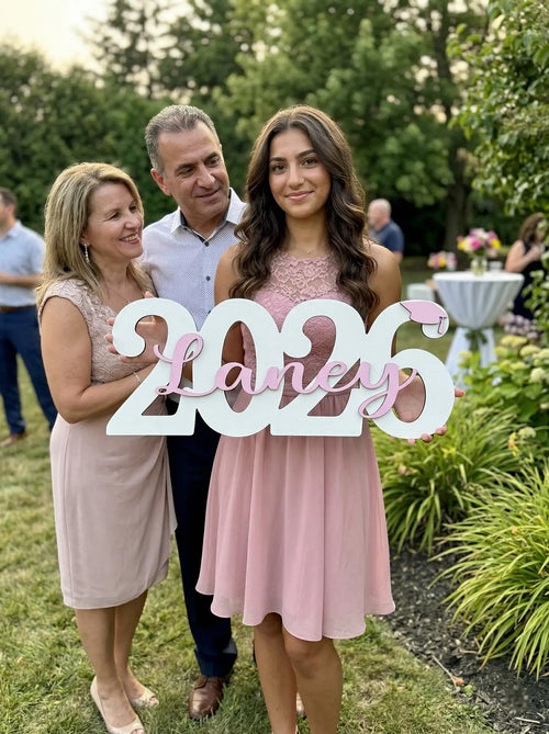 Family holding a '2026 Laney' sign outdoors in a garden setting.