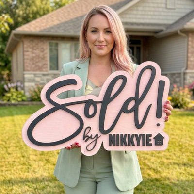 Realtor holding a pink Sold sign with her name in front of a house